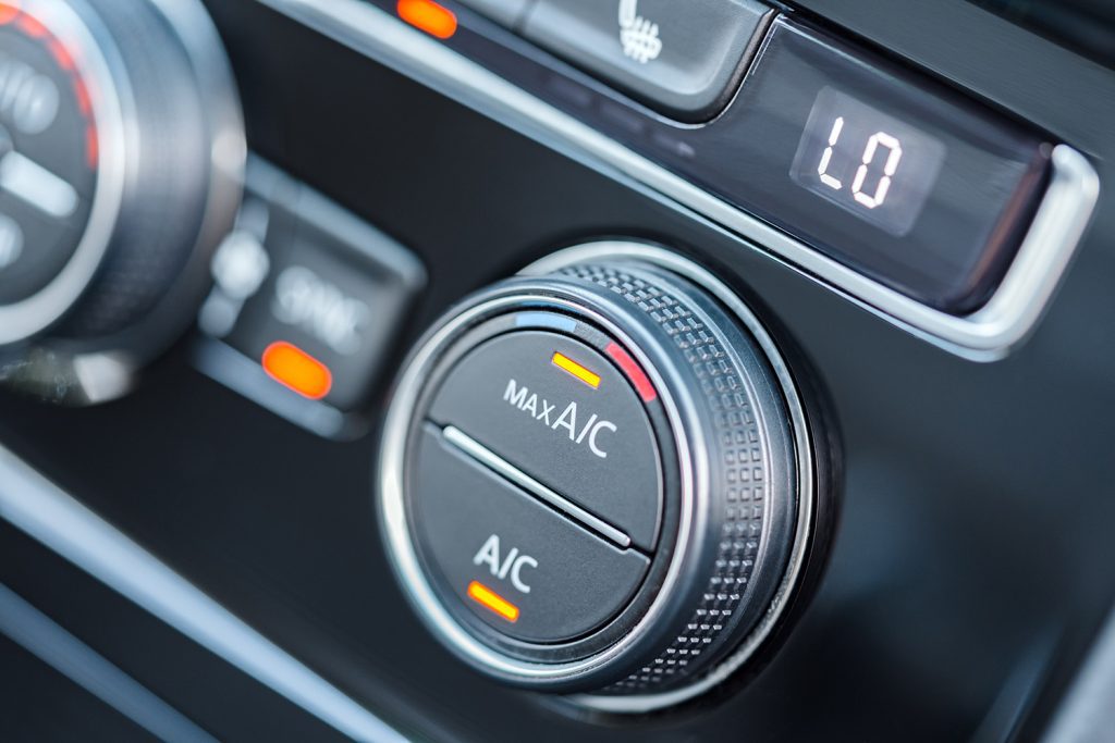 A black knob on a car's dashboard for the air conditioning, with a yellow light indicating it's on max AC.