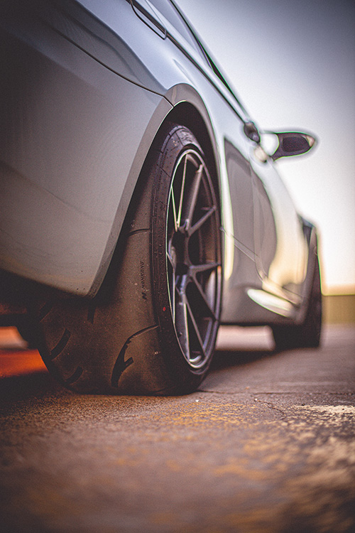 A rear tire on a car that is bald and cracking.