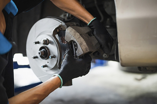 An auto mechanic installing car front brake caliper and brake pads.