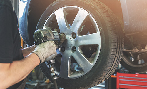 A mechanic screws the lug nuts of a wheel on a car at a tire shop.