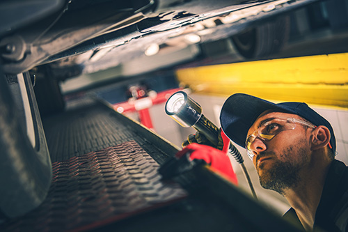 A mechanic using a flashlight to check a car's undercarriage.