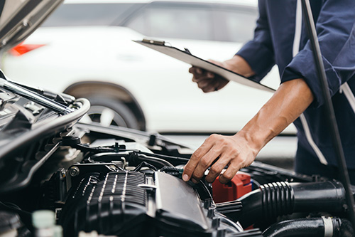 A mechanic with a clipboard checking the engine of a car.