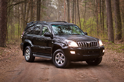 A black SUV with its headlines on parked in the forest.