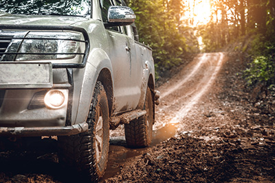 A silver pickup truck driving through the mud in the woods.