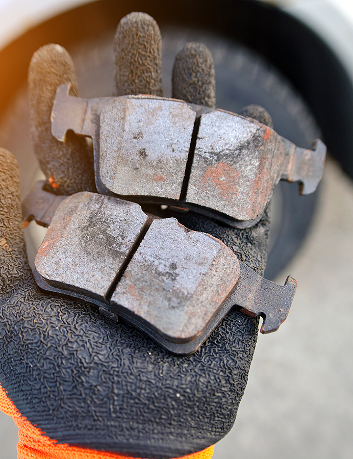 Mechanic holds bad brake pads in hand, replacing worn uneven defective pads